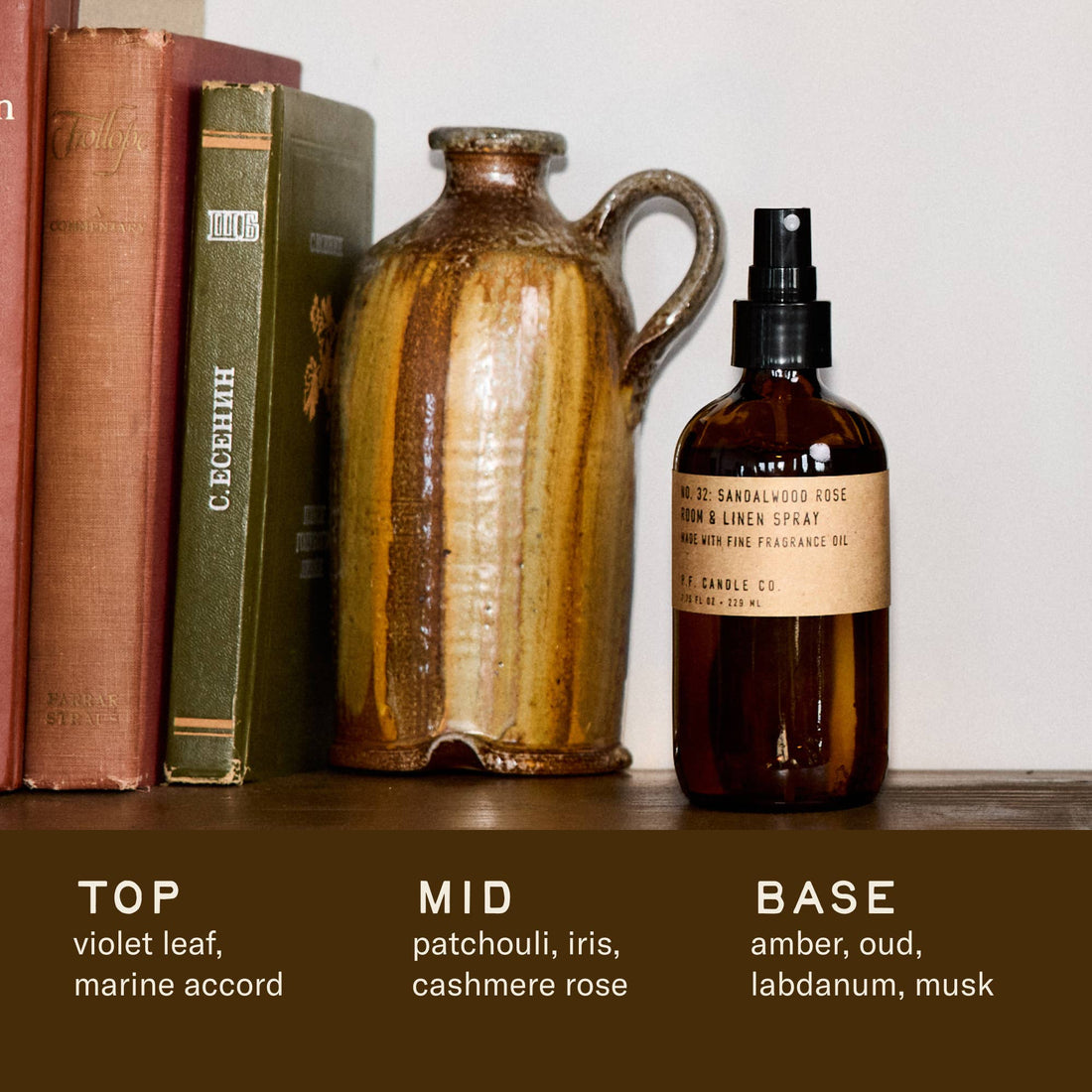 Bottle of Sandalwood Rose Room & Linen Spray on a shelf with a ceramic jug and books. 