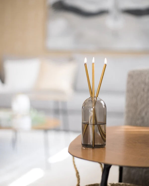 image of lit gold everlasting candles in a smokey grey vase.