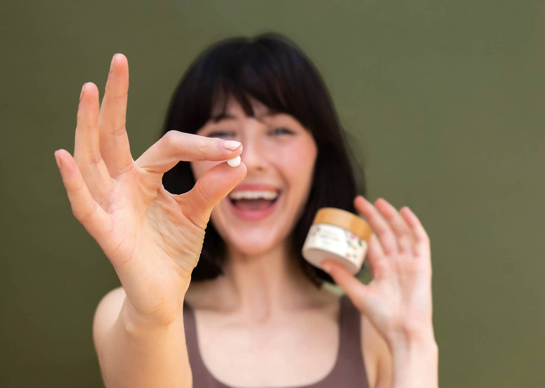 Woman holding up a tanit toothpaste tablet against a green background