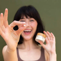 Woman holding up a tanit toothpaste tablet against a green background