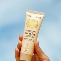 Hand holding a tube of Tannit SPF 50 sunscreen cream against a blue sky background