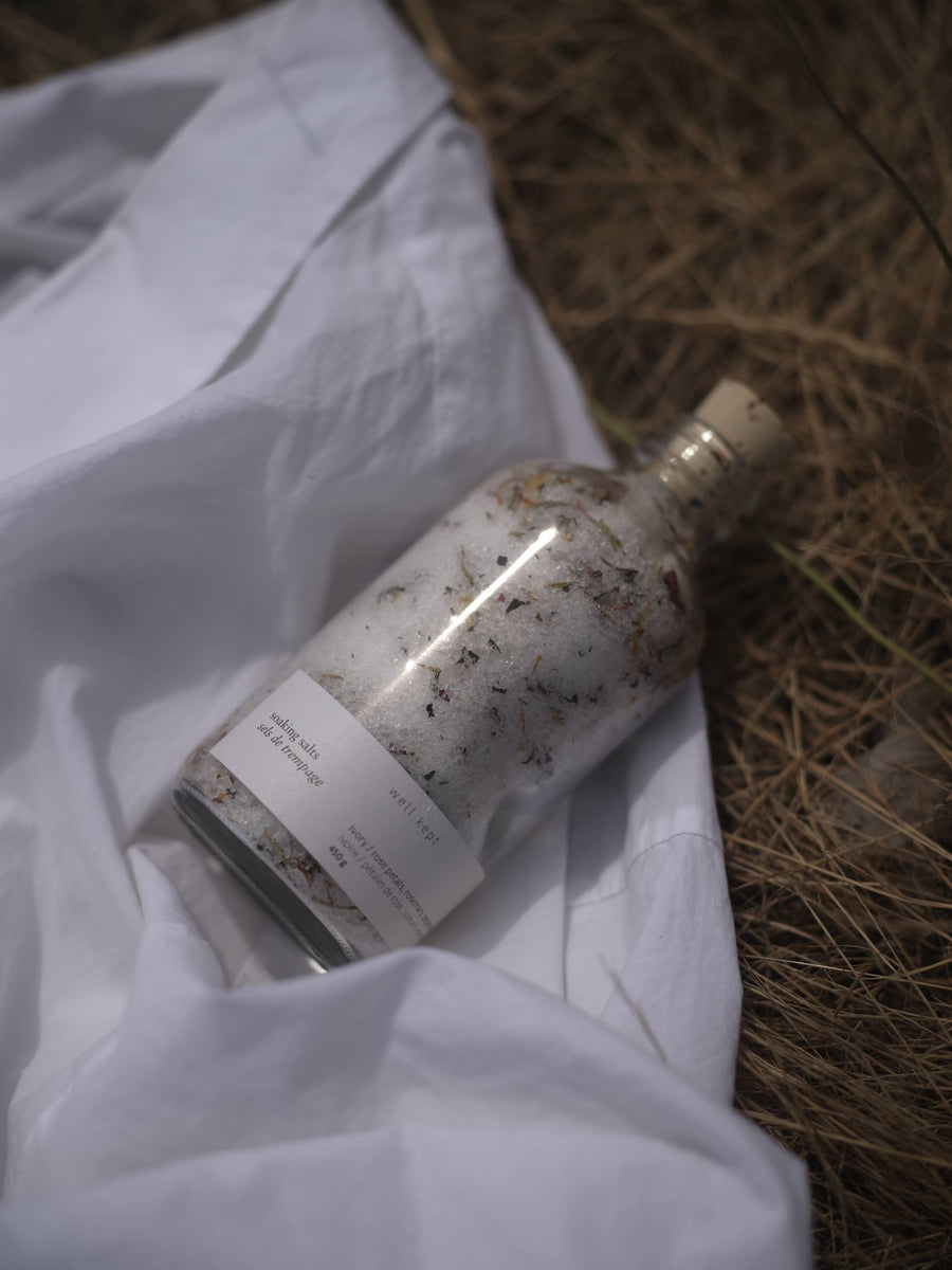 a bottle of well kept soaking salts on a white cotton fabric laying on a bed of dried grasses
