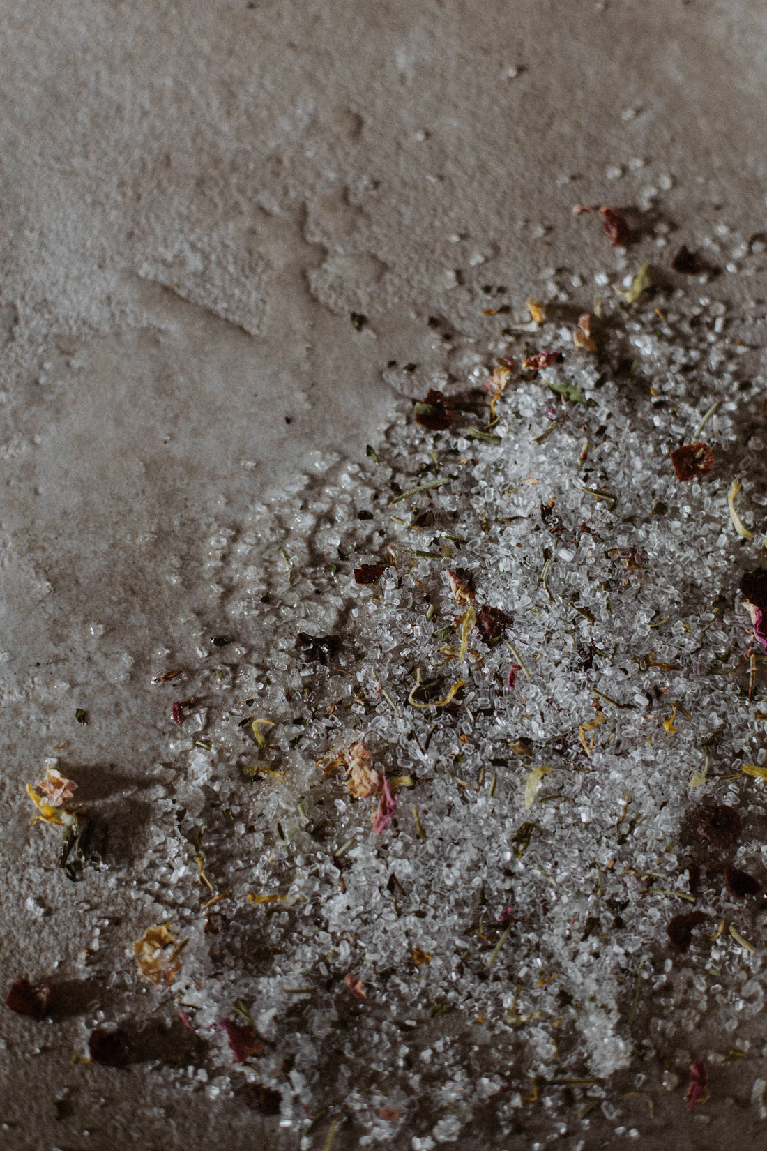 Well Kept soaking salts spilled out onto a beige stone surface showing the salts and botanicals texture