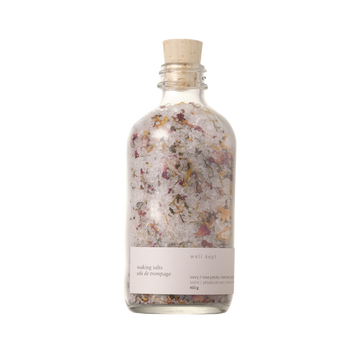 A clear glass bottle with a cork stopper, labeled 'Soaking Salts - Thrive' by Well Kept.