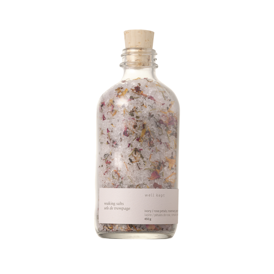 A clear glass bottle with a cork stopper, labeled 'Soaking Salts - Thrive' by Well Kept.
