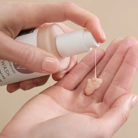 Hand holding a bottle of Wildcraft Cream Cleanser pumping product out onto their other hand against a beige background