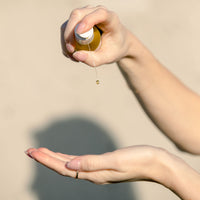 Garden City Essentials cleansing oil being pumped into an open hand. The shadow of a woman's head is seen in the background.
