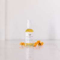 Garden City Essentials cleansing oil with dried calendula flowers on a reflective surface with soft white background