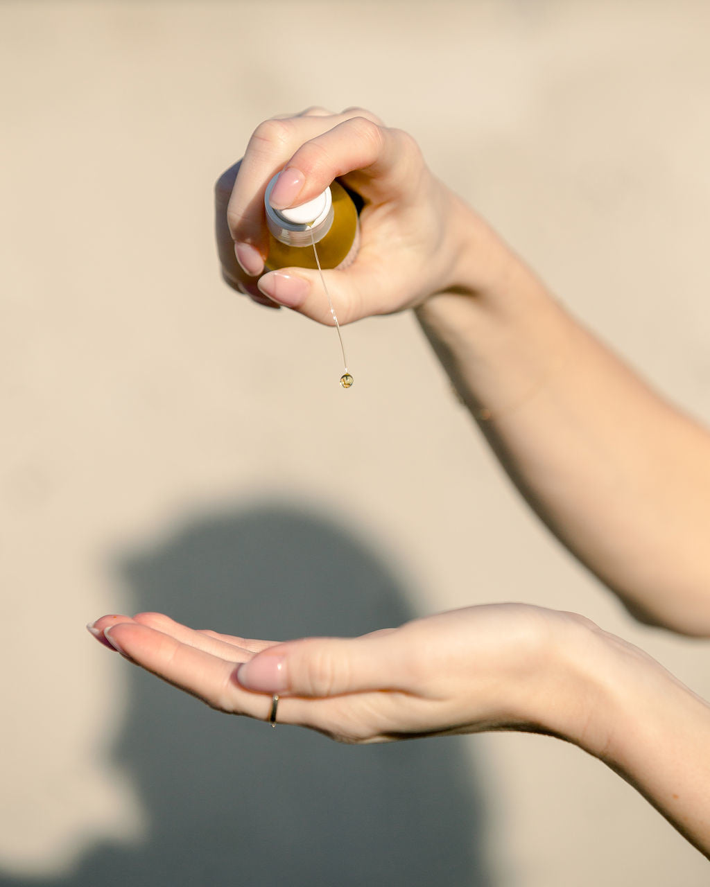 Garden City Essentials cleansing oil being pumped into an open hand. The shadow of a woman's head is seen in the background.